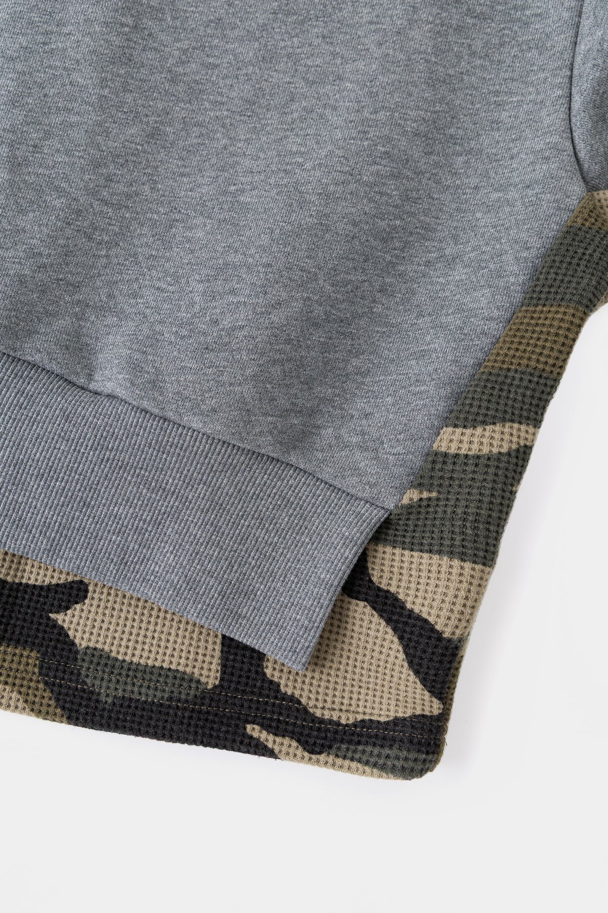 Detail of the waffle camo layer emerging under the ribbed hem.