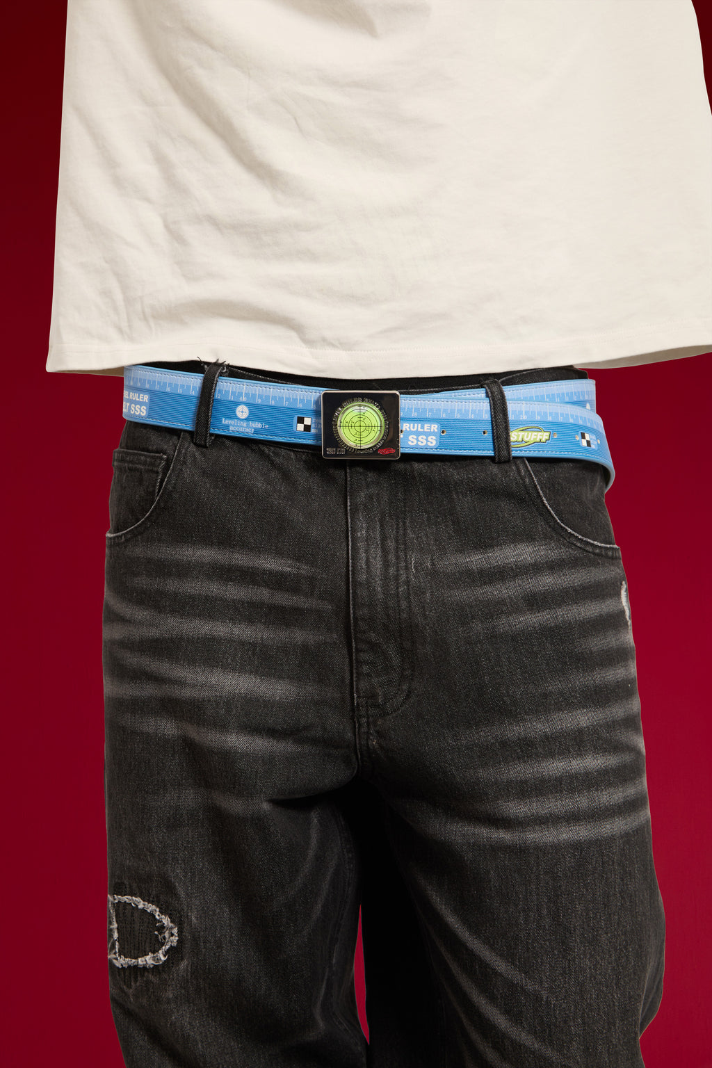 Swappable Level and Ruler Belt worn on a model through the loops of black jeans, close-up of the spirit level buckle, one of two that snap on and off.