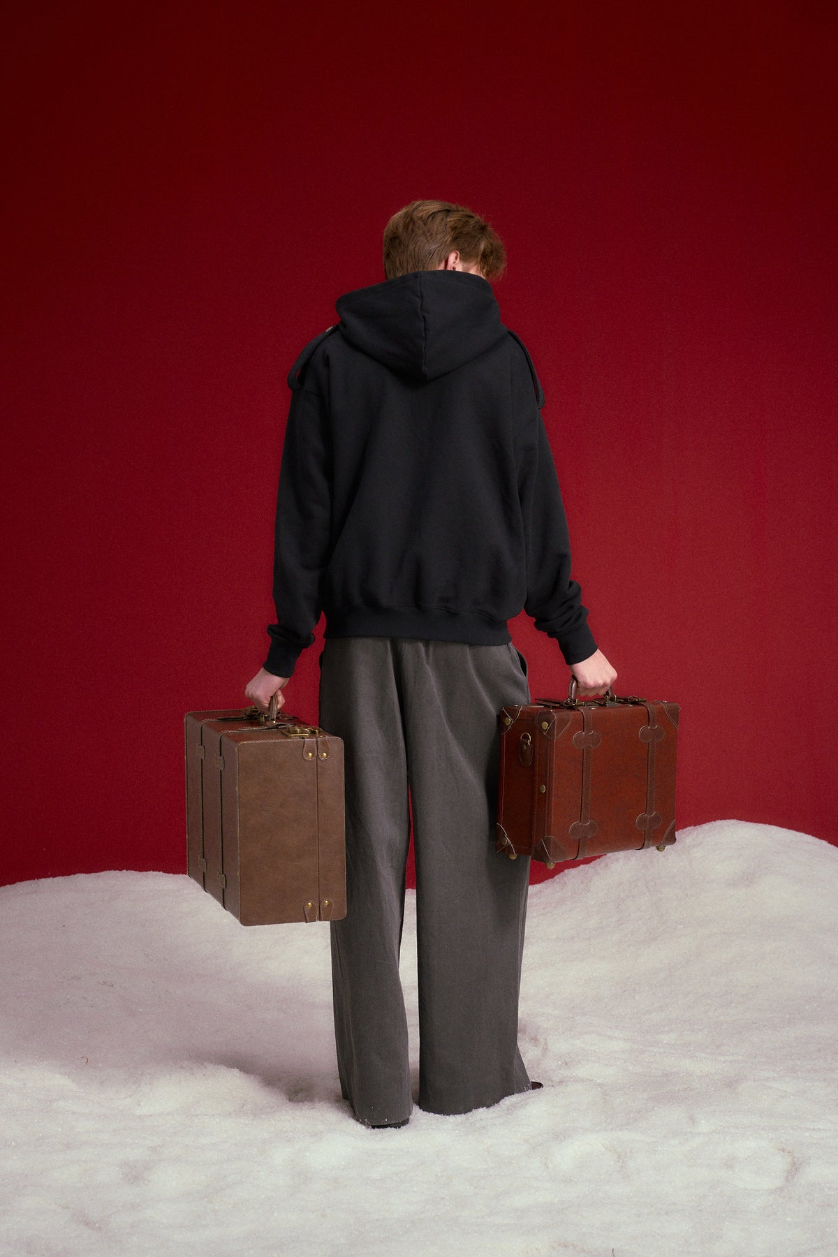Lobby Boy Hoodie in black, with concierge chest closures and shoulder epaulettes. Worn on a model, full-length back view.