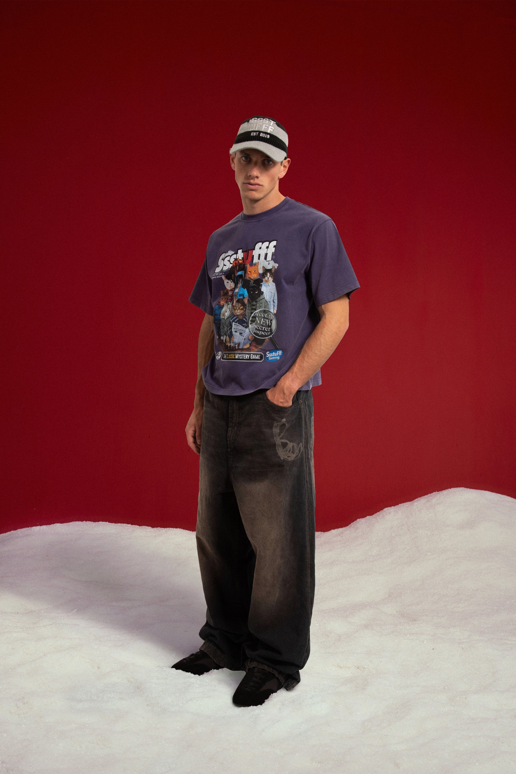 Mystery Cats Tee in washed purple, printed with the whole cast of the case redrawn as cats. Worn on a model with the Newspaper Spy Cap, full-length front view.