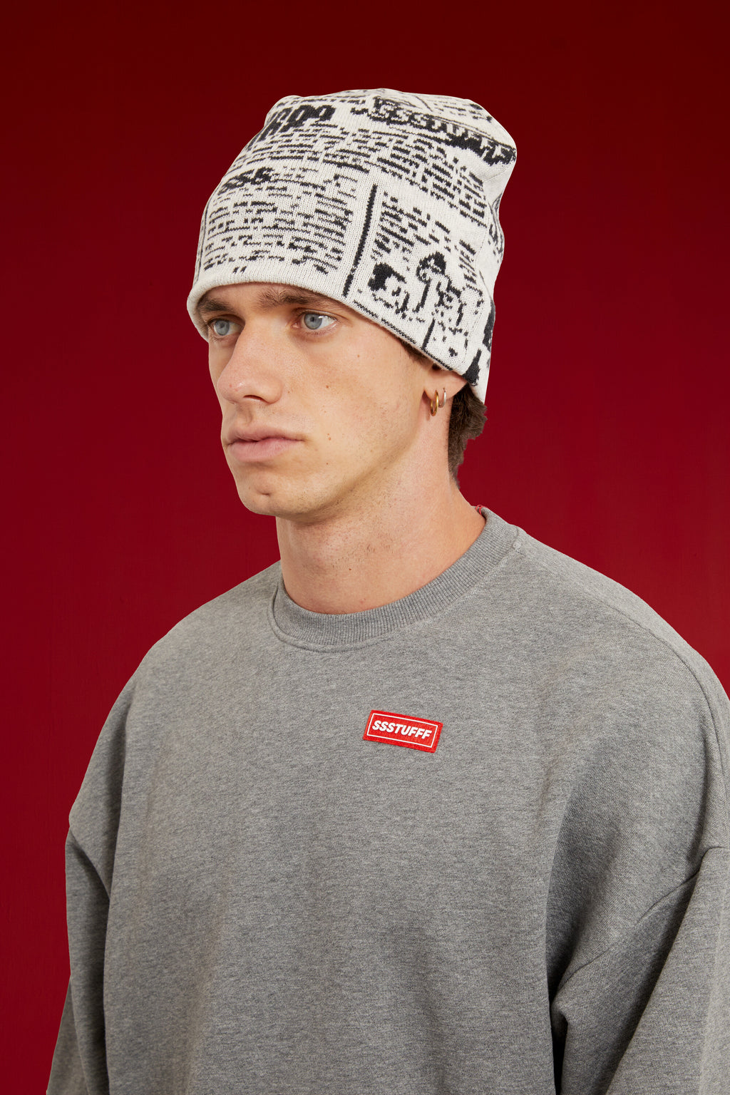 Newspaper Spy Beanie in newsprint jacquard, with two eye holes knitted into the front. Worn on a model, close-up detail, front of the cap.