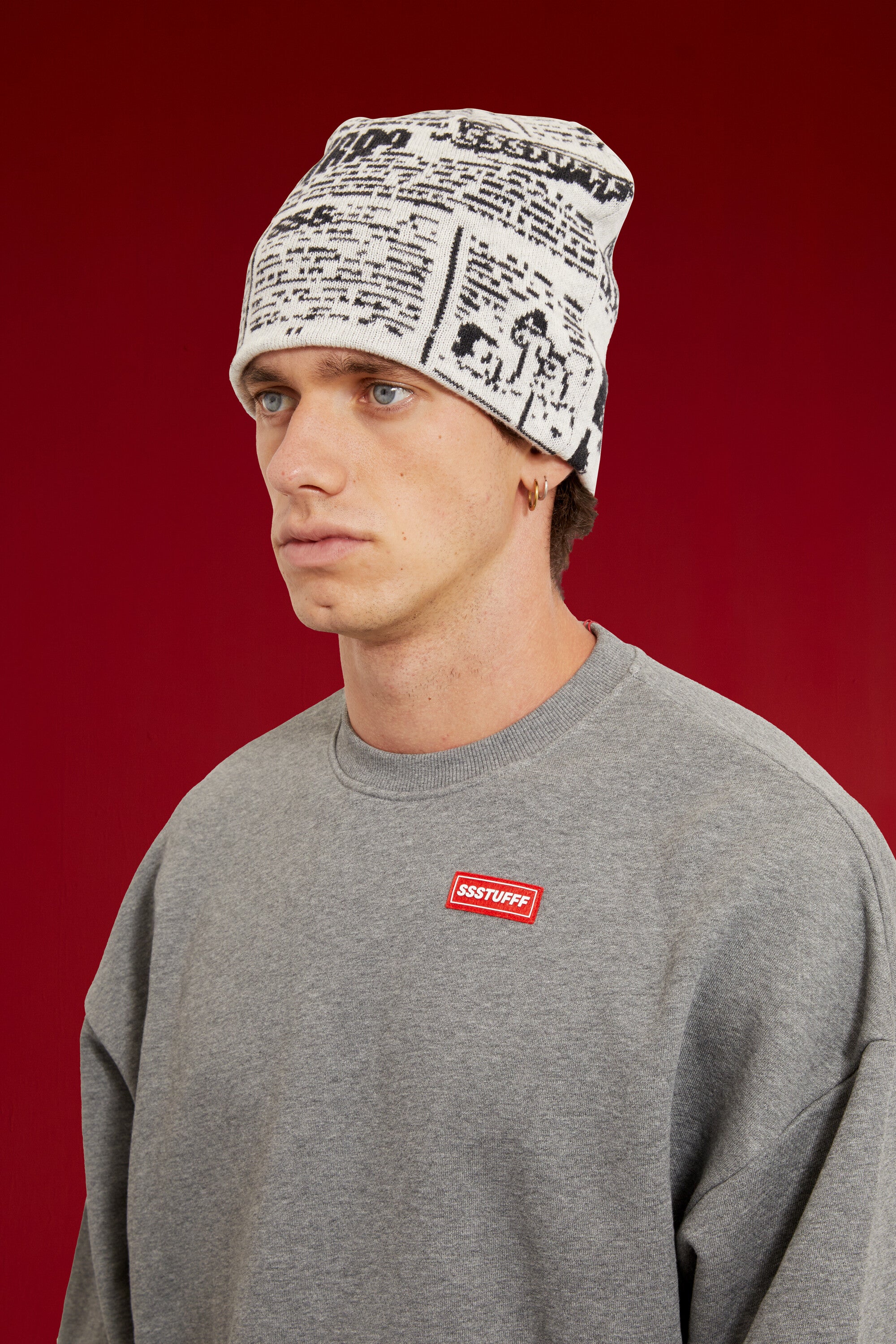 Newspaper Spy Beanie in newsprint jacquard, with two eye holes knitted into the front. Worn on a model, close-up detail, front of the cap.