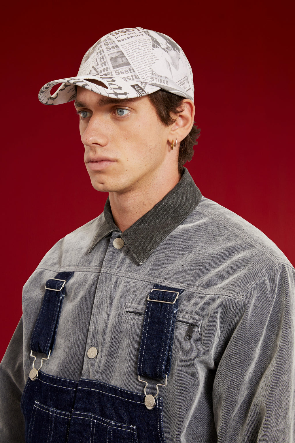 Newspaper Spy Cap in all-over newsprint print, a six-panel cap with a curved brim. Worn on a model, close-up detail, front of the cap.