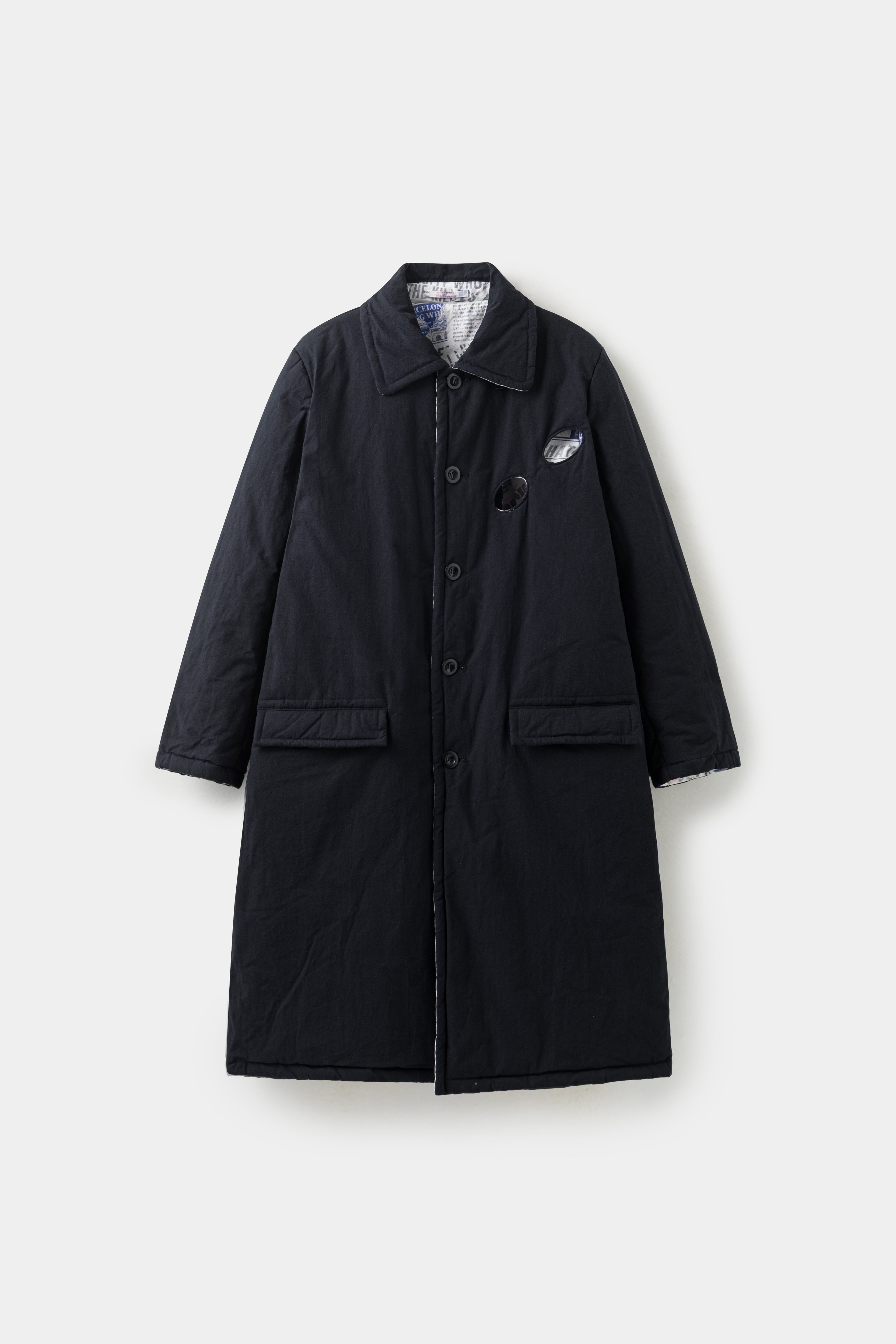 The Newspaper Spy Coat reversed to its plain black side, with flap pockets and a concealed placket.