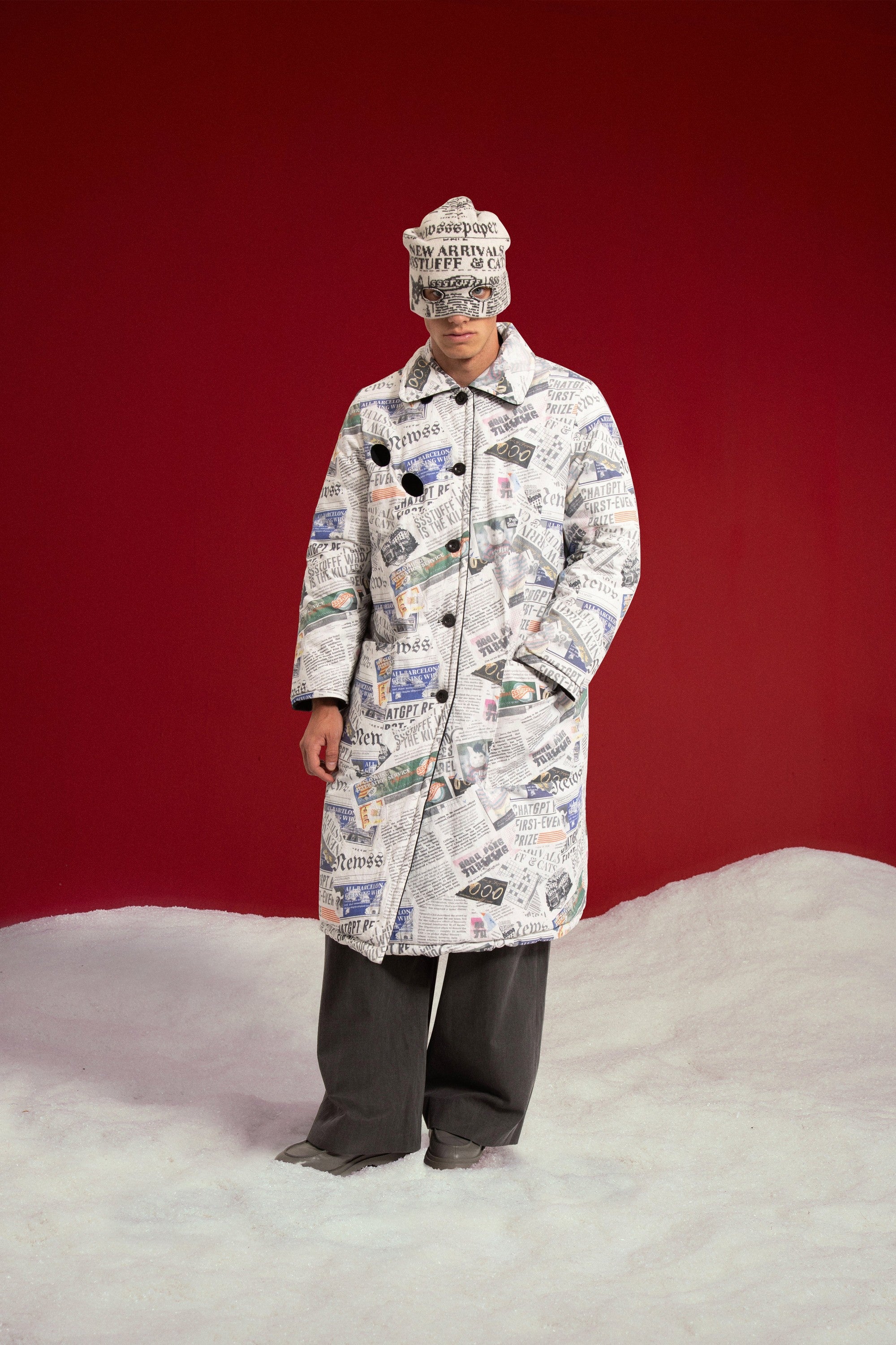 Newspaper Spy Coat on its newspaper print side, worn with the Newspaper Spy Beanie. Worn on a model, full-length front view.