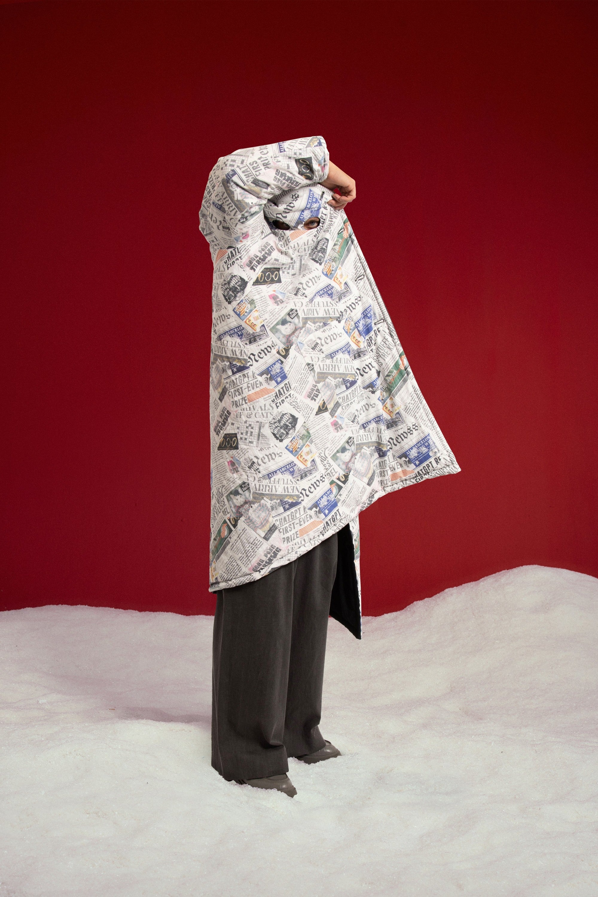Newspaper Spy Coat held open by the model, newspaper print outside and the plain black reverse showing inside. Worn on a model, full-length view.
