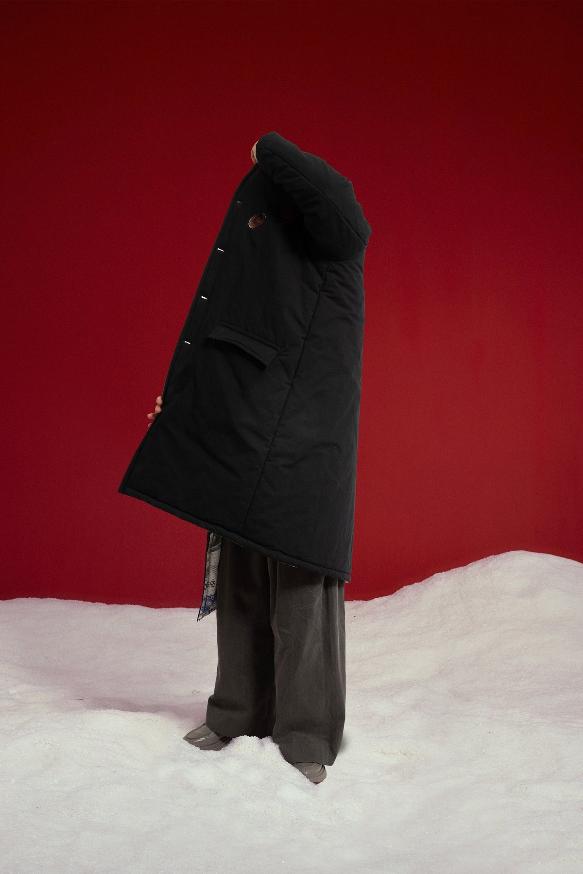 Newspaper Spy Coat on the black side, held open to show the newspaper print inside. Worn on a model, full-length side view.
