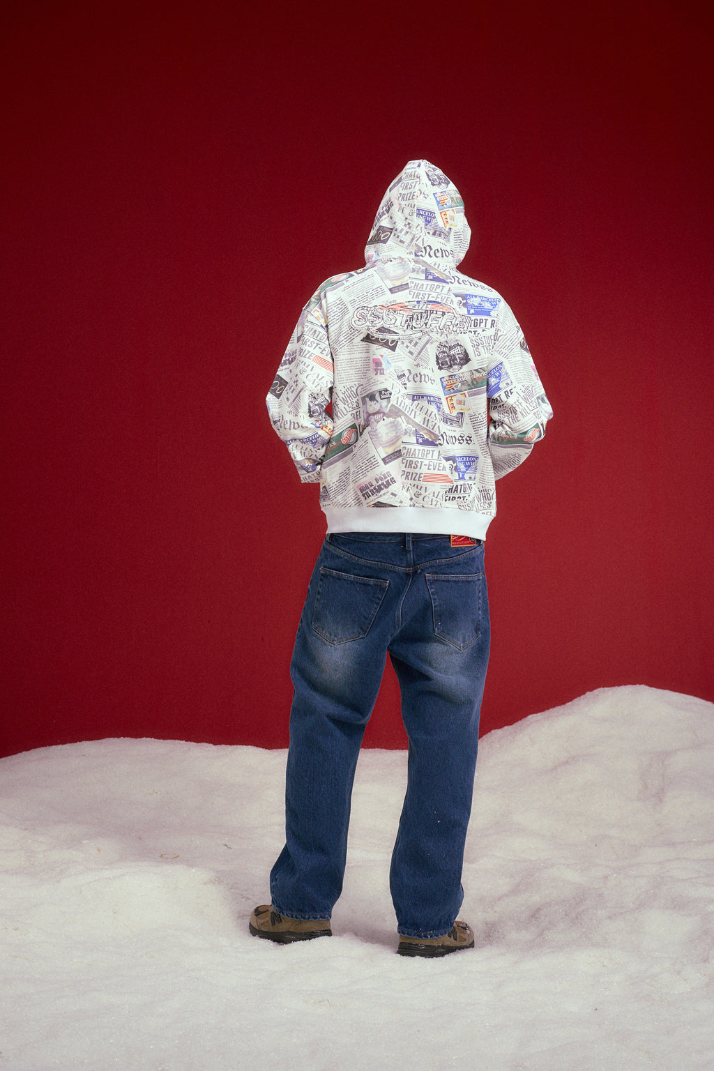 Newspaper Spy Hoodie, a zip-up hoodie printed all over with newsprint. Worn on a model, full-length back view.