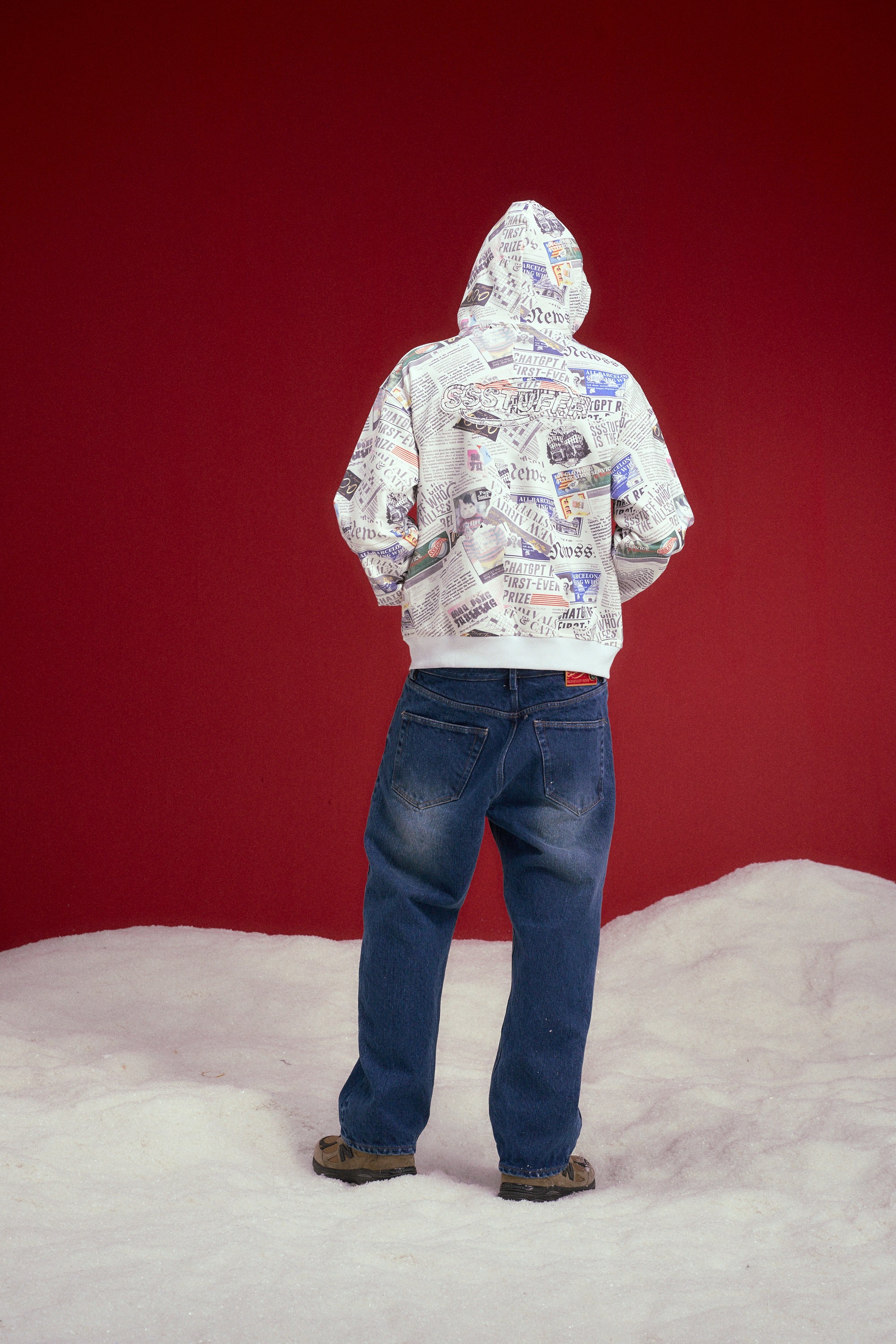 Newspaper Spy Hoodie, a zip-up hoodie printed all over with newsprint. Worn on a model, full-length back view.