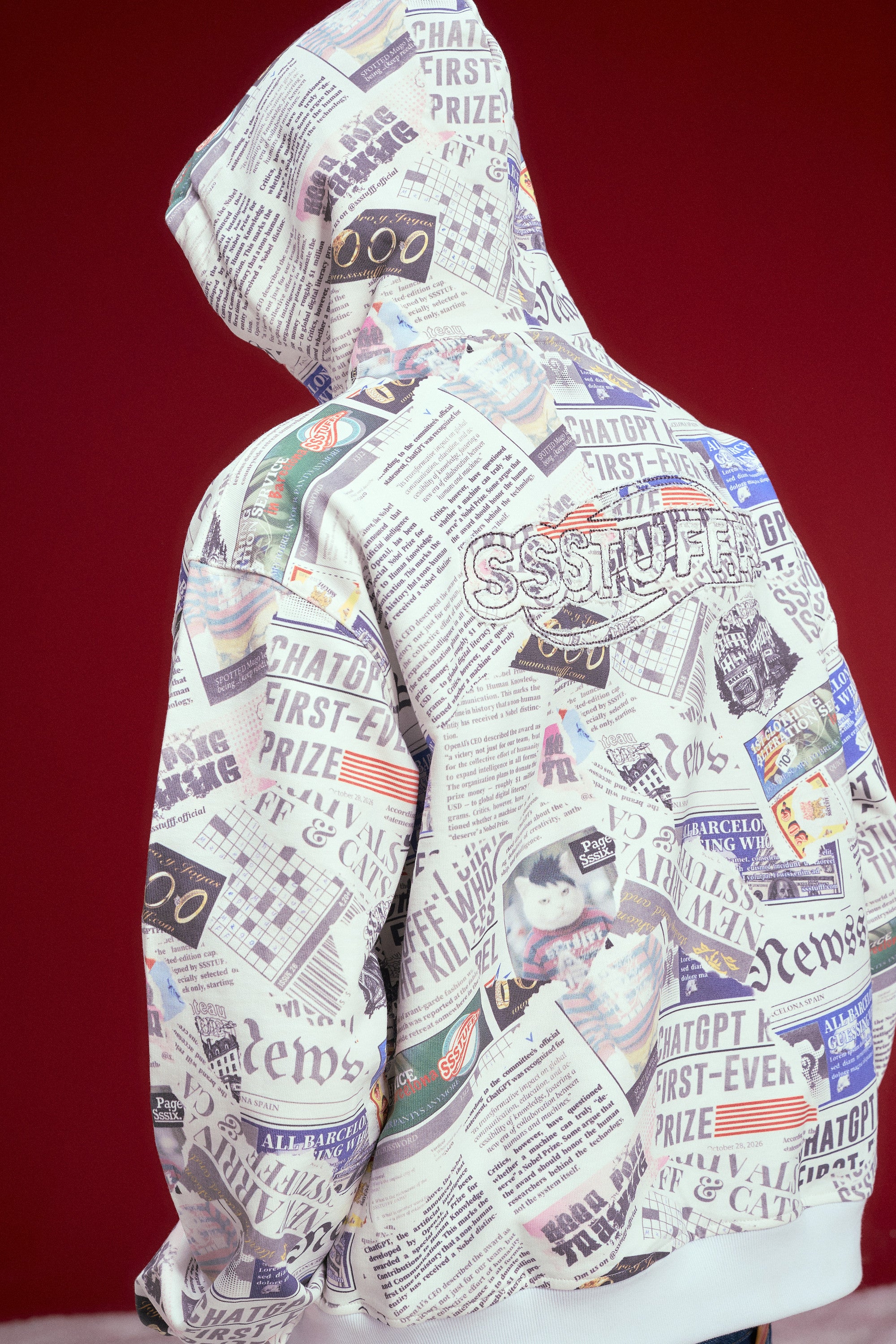 Newspaper Spy Hoodie, a zip-up hoodie printed all over with newsprint. Worn on a model, full-length side view.