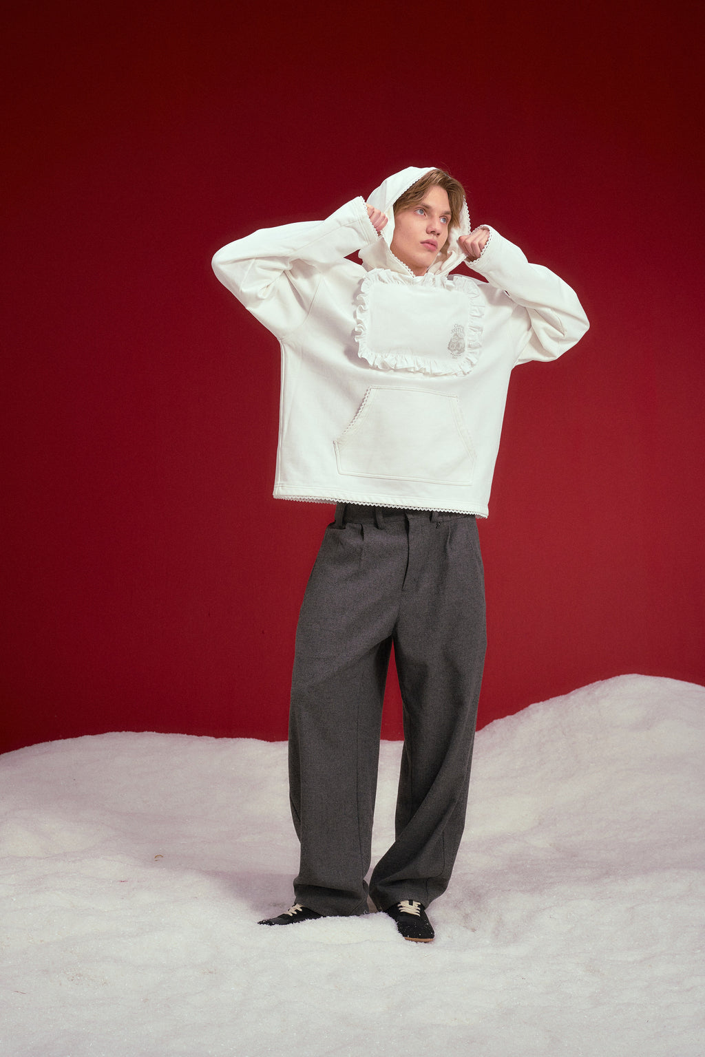 Pillow Hoodie in off-white, with a padded pillow patch sewn onto the chest. Worn on a model, full-length front view, hood up.