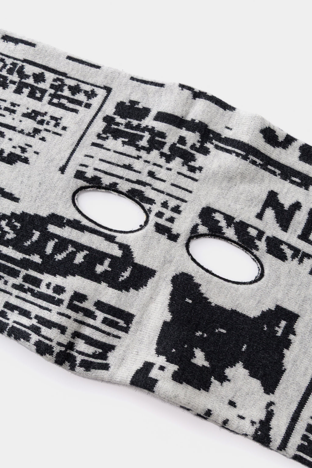 Close-up of an eye hole knitted into the newsprint, for watching from behind the paper.