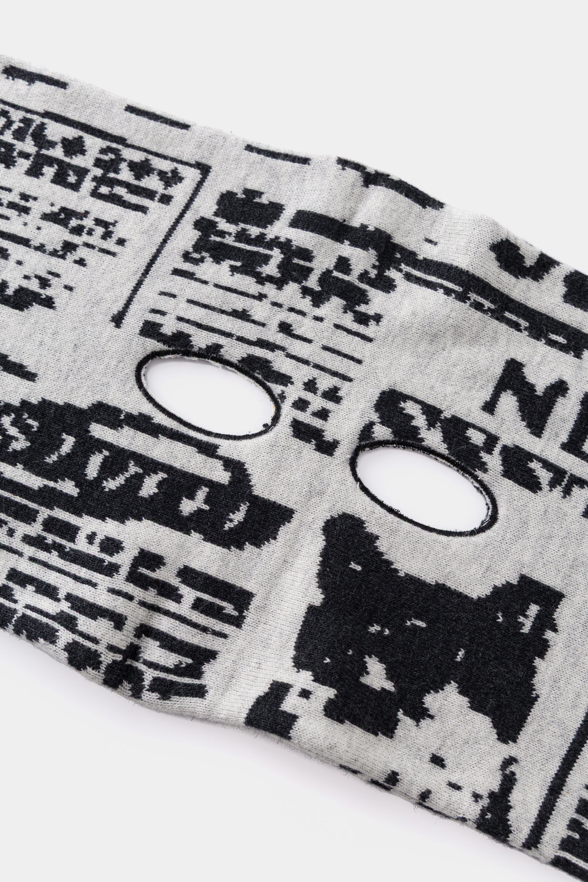 Close-up of an eye hole knitted into the newsprint, for watching from behind the paper.