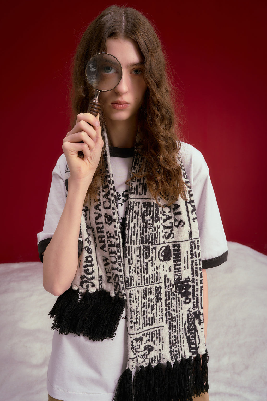 Spy Knitted Scarf in newsprint jacquard, a long scarf with black fringing at both ends. Worn on a model, waist-up view.