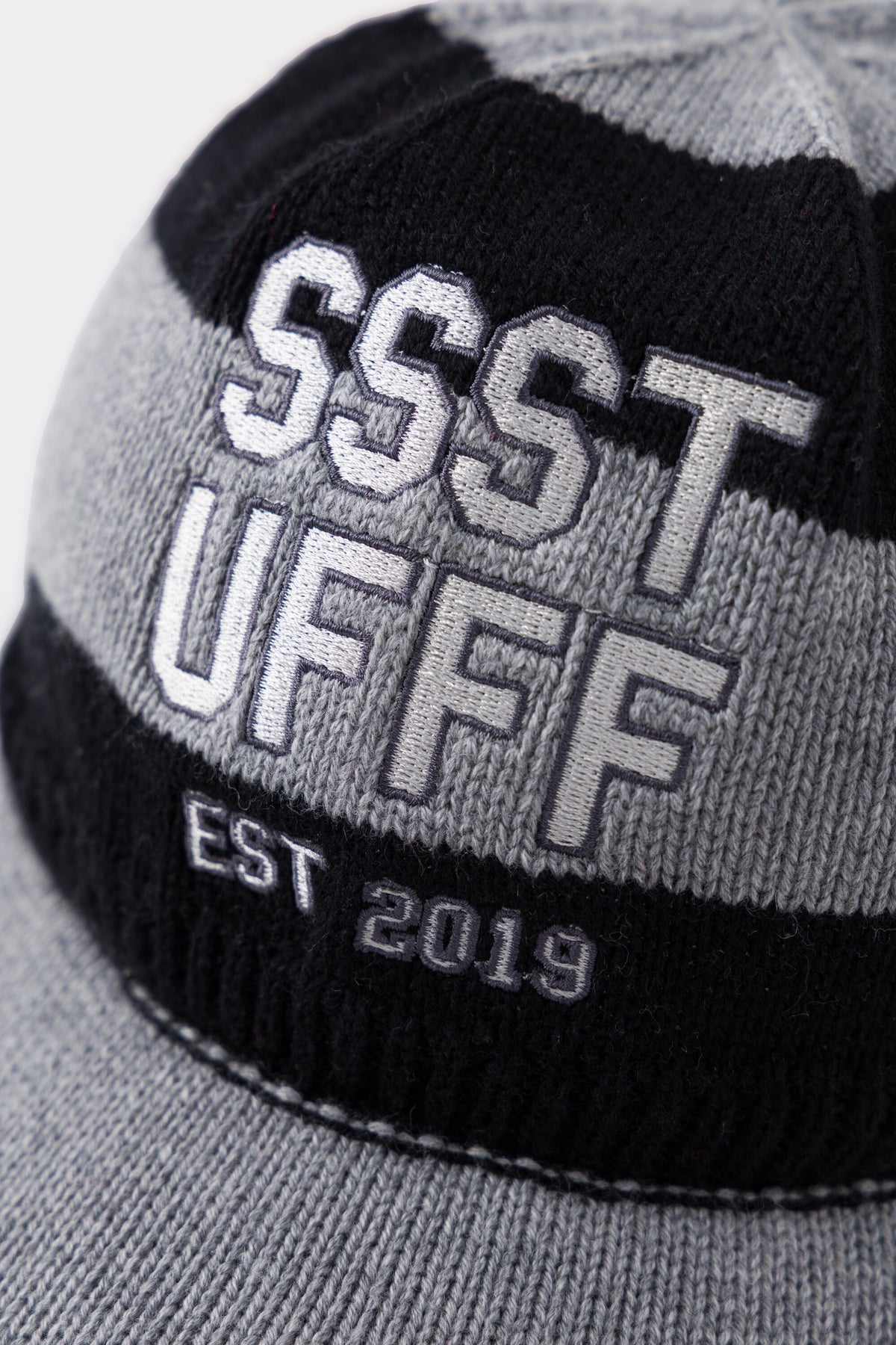 Close-up of the raised SSSTUFFF EST 2019 varsity embroidery across the black and grey stripes.