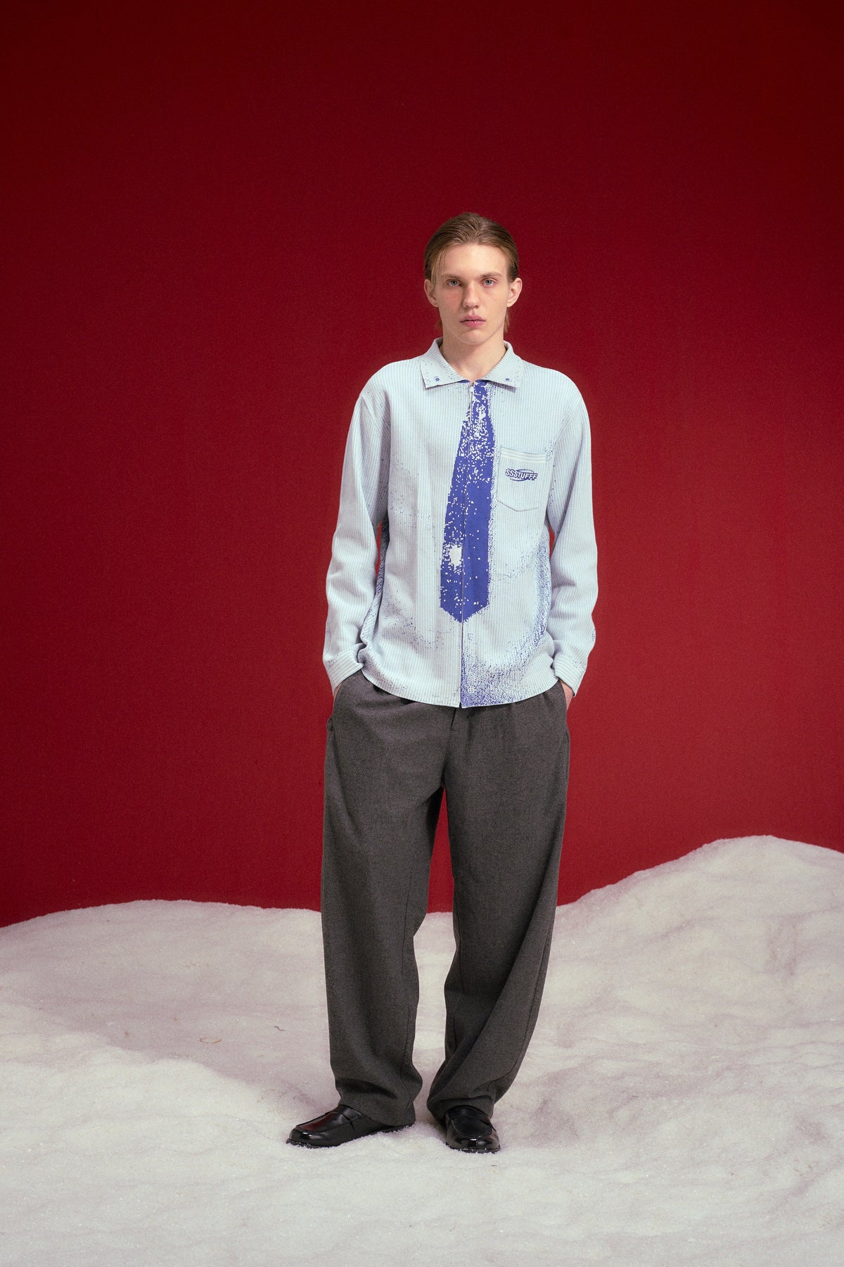 Tie Knit in pale blue, a knitted polo with the necktie knitted straight onto the front. Worn on a model, full-length front view.