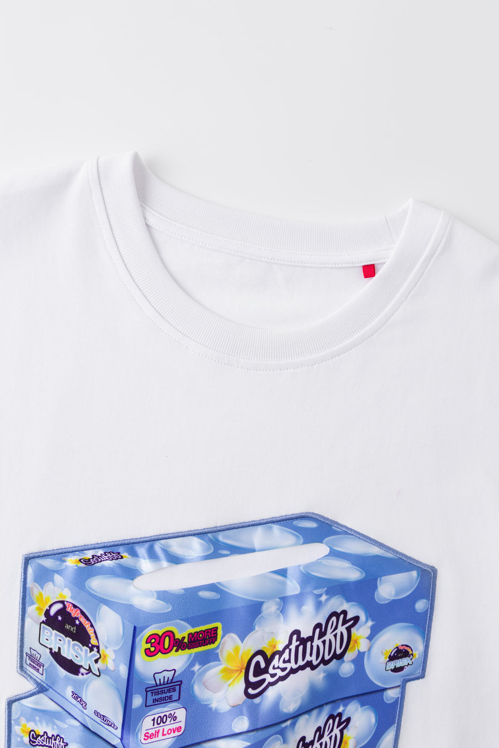 Close-up of the white tee's neckline and red woven label, above the top of the tissue box print.