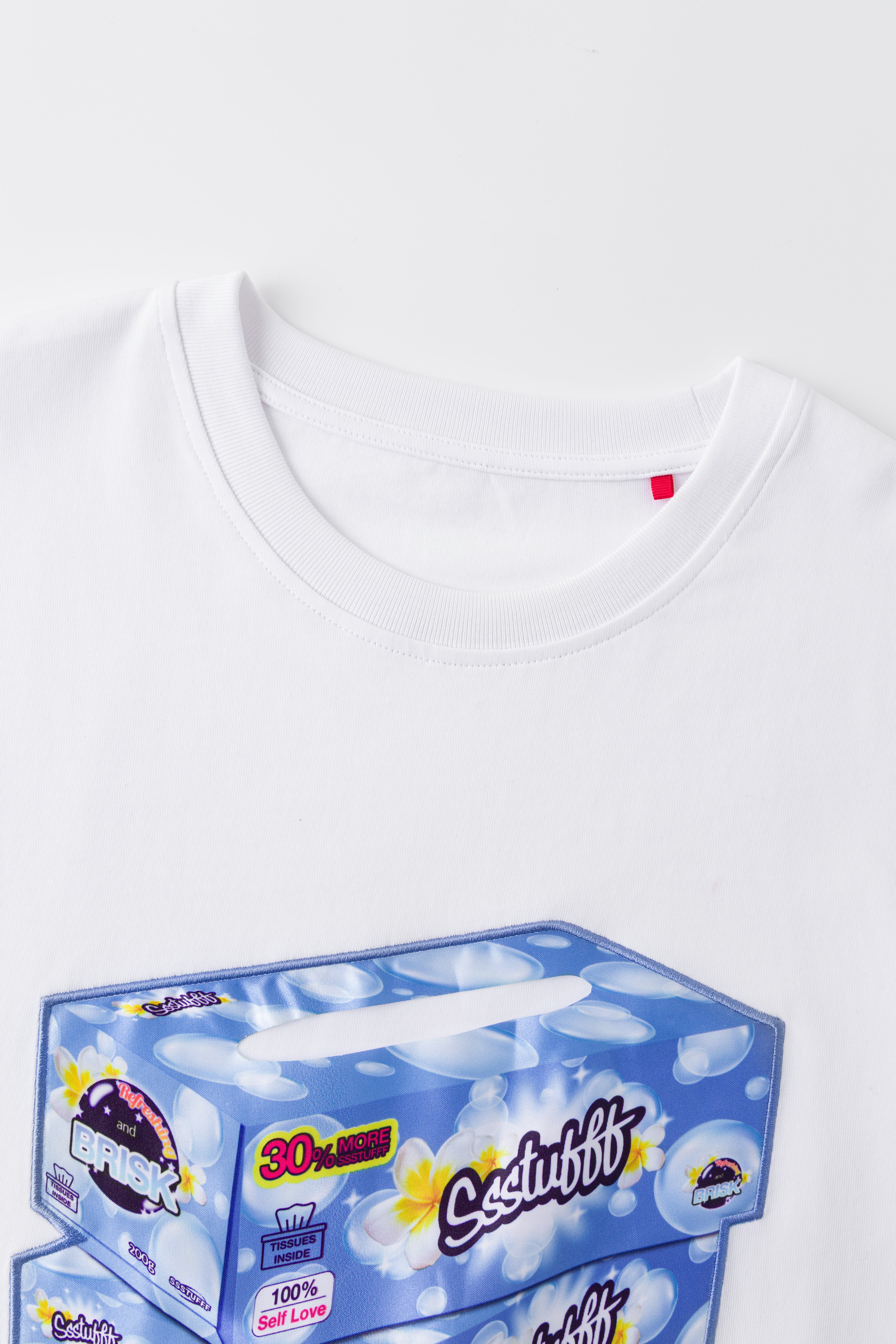 Close-up of the white tee's neckline and red woven label, above the top of the tissue box print.