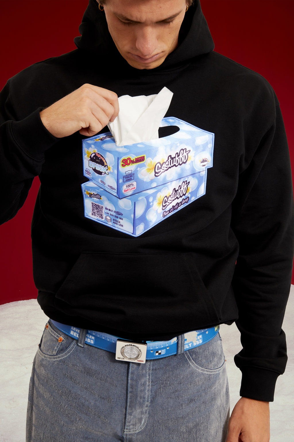 Tissue Hoodie in black, with a 3D tissue box patch sewn onto the chest. Worn on a model, waist-up view.