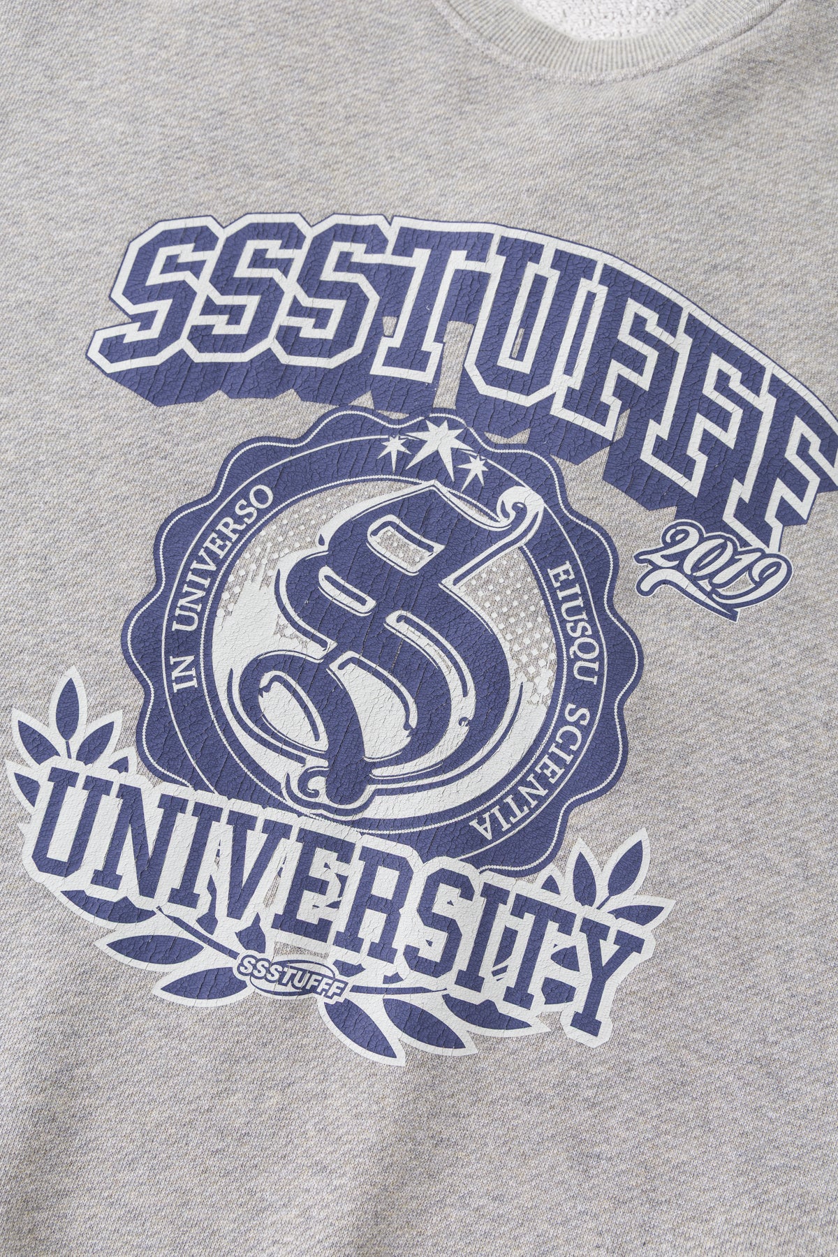 Detail of the SSSTUFFF University crest, printed in navy with a laurel wreath.
