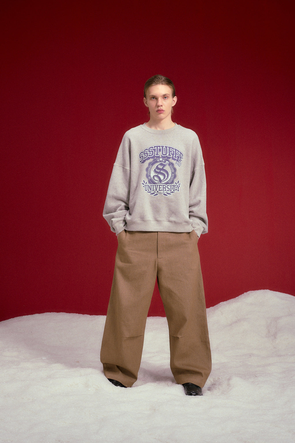 University Logo Crewneck in grey marl, printed with the SSSTUFFF University crest. Worn on a model, full-length front view.