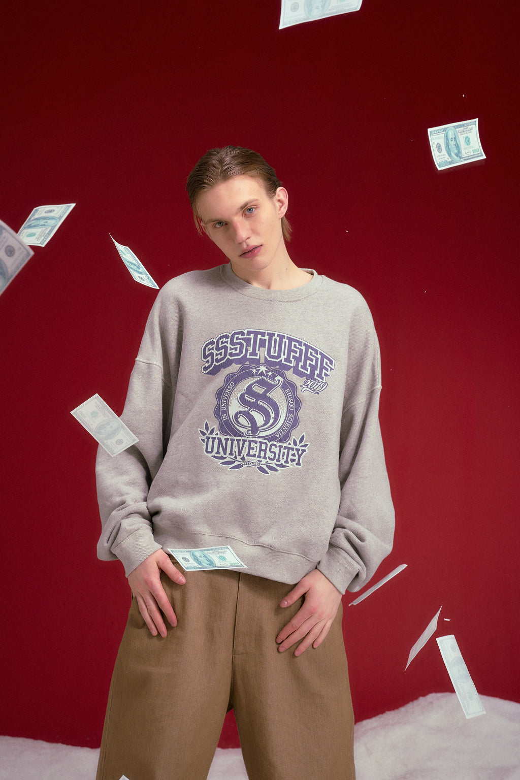 University Logo Crewneck in grey marl, printed with the SSSTUFFF University crest. Worn on a model, waist-up view, throwing banknotes.