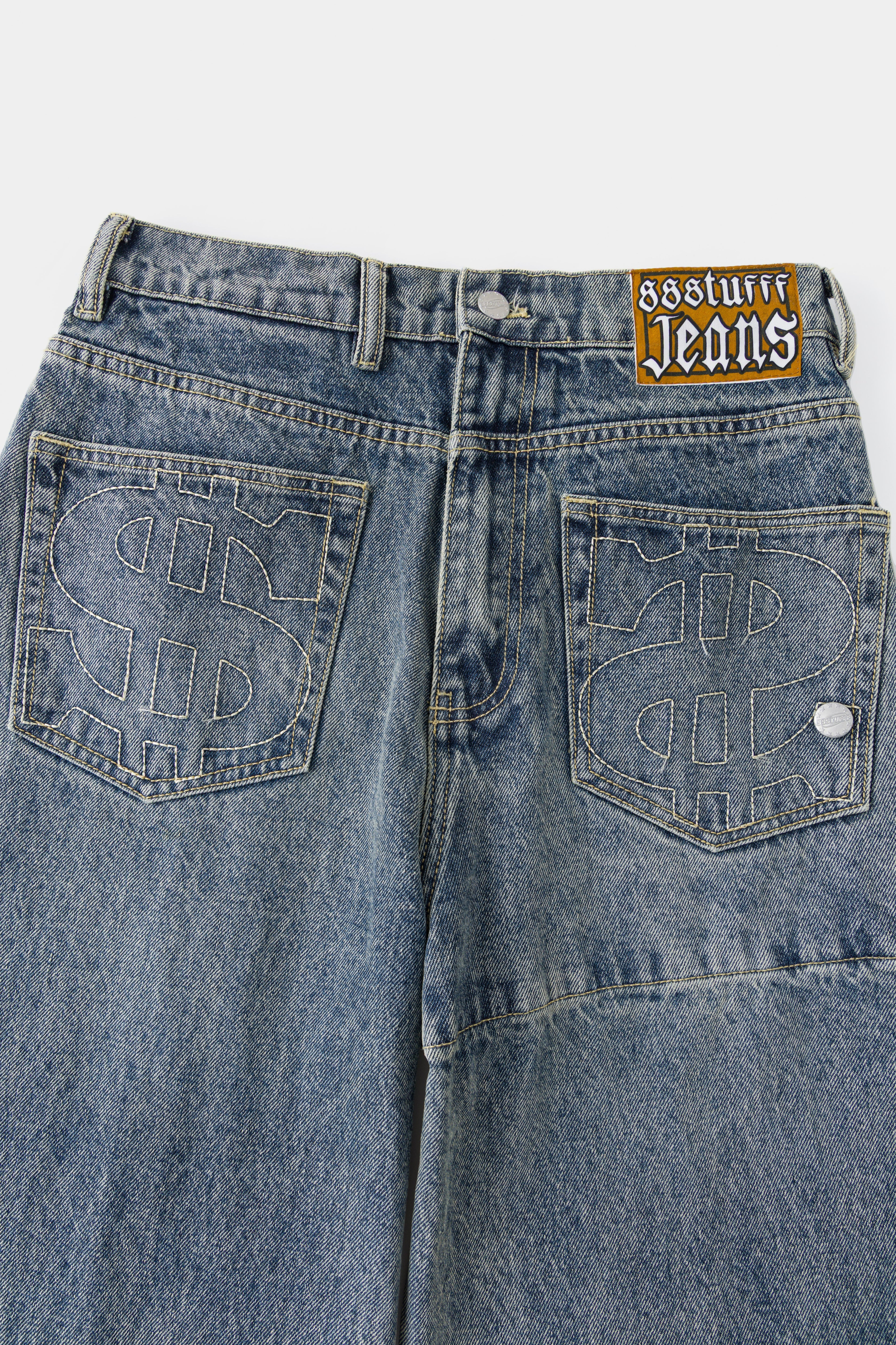 Close-up of the back pockets with embroidered $ logos and the Ssstufff Jeans label at the waistband.