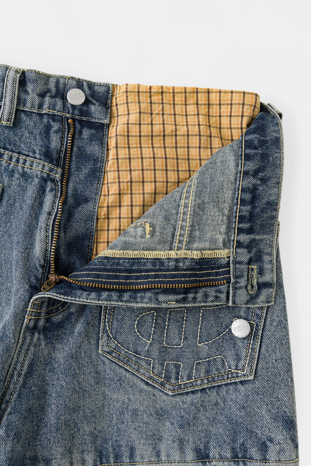 Close-up of the front fly opened, showing the checked underwear layer inside the waistband.