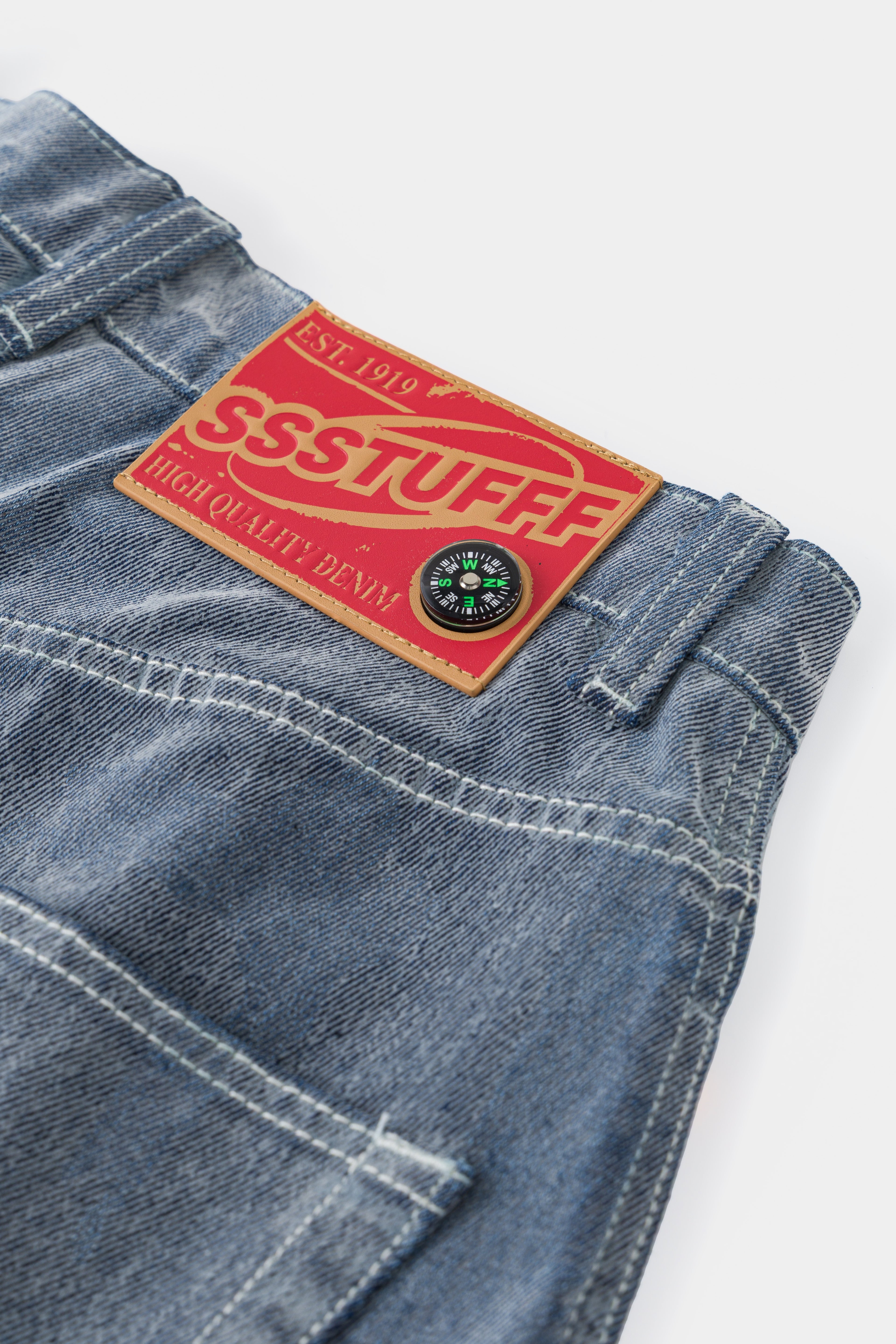 Close-up of the red SSSTUFFF Est. 1919 denim label on the flocked back waistband.