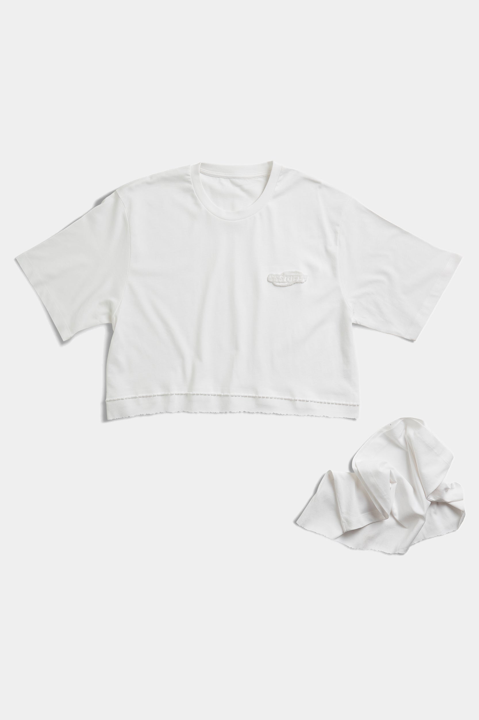 Cropped version of the white FUWARI Embroidery Tee laid flat beside the detached lower panel