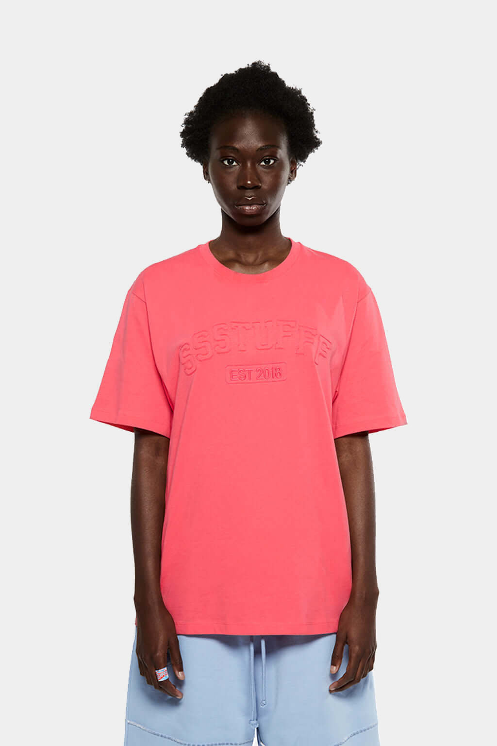 Model wearing the coral red University Patchwork Tee with light blue shorts