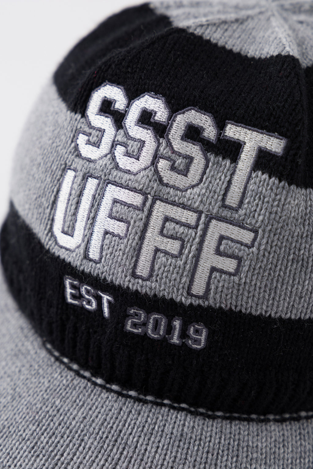 Close-up of the raised SSSTUFFF EST 2019 varsity embroidery across the black and grey stripes.