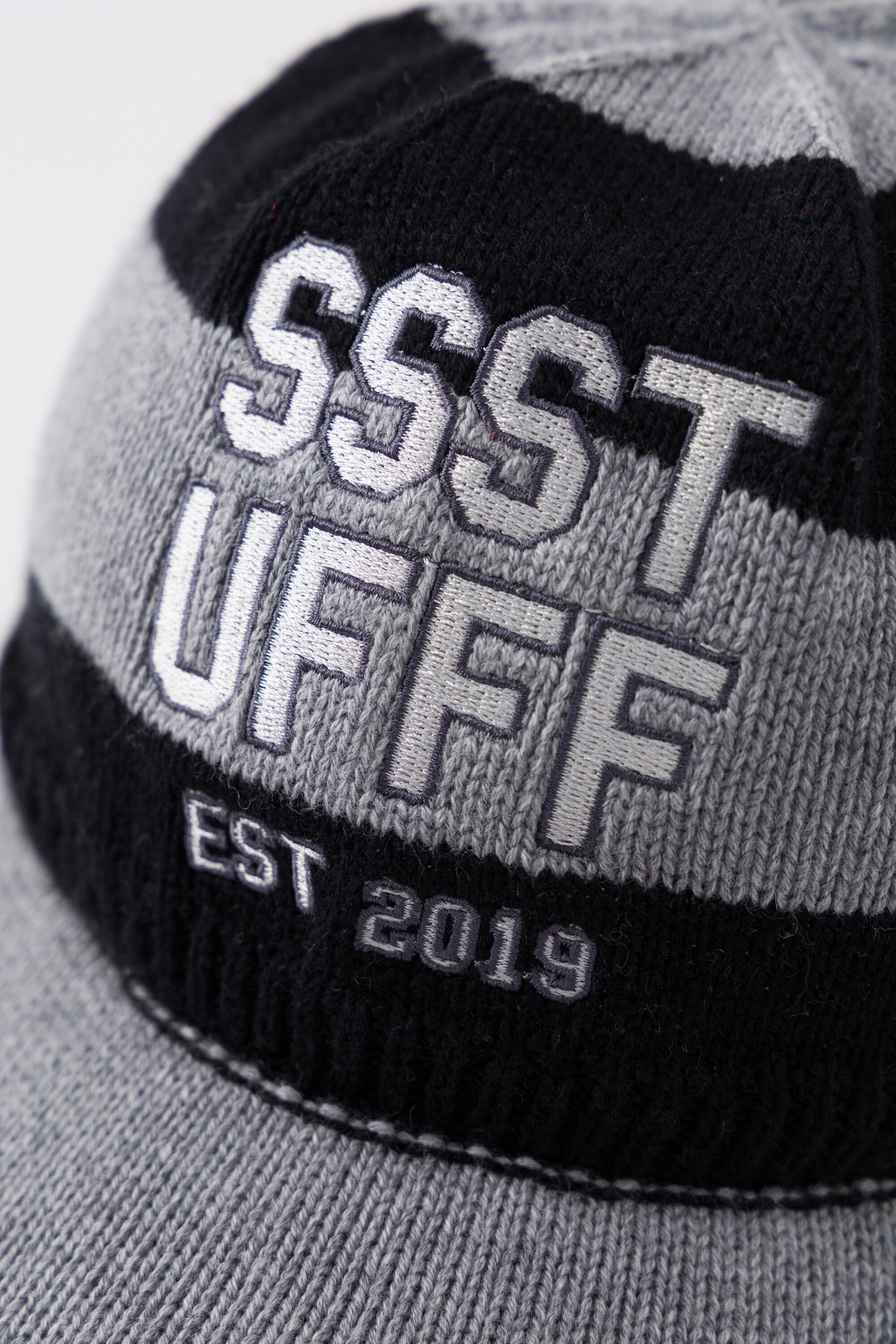 Close-up of the raised SSSTUFFF EST 2019 varsity embroidery across the black and grey stripes.